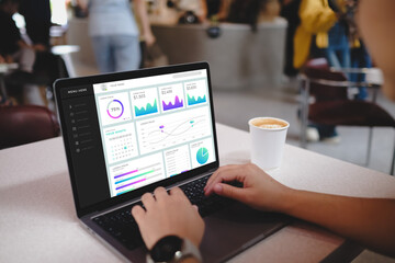 Person analyzing colorful data charts on a laptop screen with coffee in a bustling cafe.