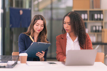 Two Asian businesswomen meet working with laptops to analyze financial charts to discuss the...