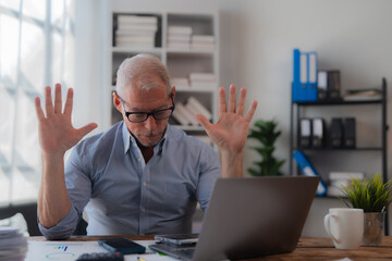 Senior businessman showing stop gesture with both hands during video call in office, sitting at...