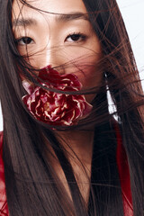Woman with flowing black hair and flower in mouth, wind blowing, beauty concept, summer breeze...