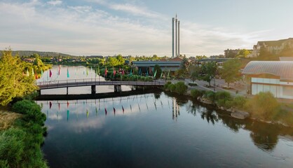 Colorful flags adorn Old Mill Bridge over a Deschutes River, reflecting the town's buildings. Peaceful morning scene. , Bend, Oregon, United States © Zenstratus