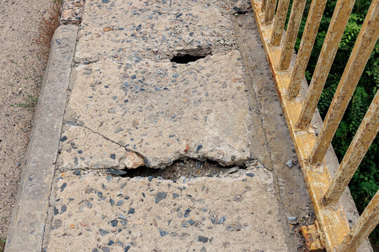 Crumbling concrete walkway with safety hazards and yellow railing