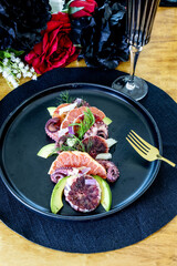 Citrus Octopus salad with blood orange and avocado on a black plate
