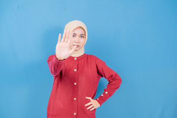 A woman wearing a red sweater and a yellow head scarf is holding her hand up in the air, as if to...