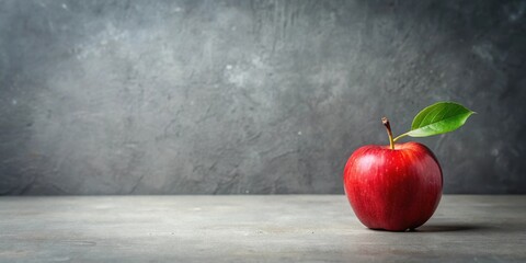 A single, vibrant red apple with a fresh green leaf rests on a neutral gray surface against a textured backdrop.