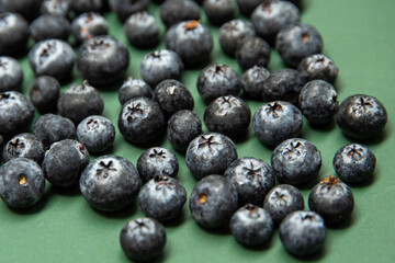 Fresh blueberries on a green surface, various berries are scattered everywhere. Blueberries have a dark blue color and a slightly rough texture.