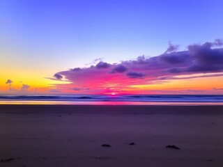Fototapeta premium A remote beach with a vibrant sunset over the horizon, glowing purple and blue with soft clouds