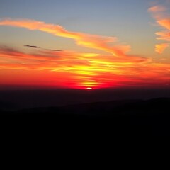 Obraz premium Intense Red and Yellow Sunset Over Hills with a Clear and Open Horizon