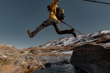 A traveler in bright clothes with a backpack on his back makes a jump from a high rock against the...