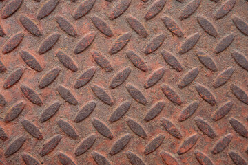 A close-up of a rusty checker plate reveals heavy, flaky rust texture, highlighting the rugged, weathered metal surface and the intricate patterns of corrosion.