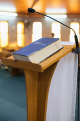 Wooden church pulpit with a blue Bible and microphone in a lit sanctuary on altar