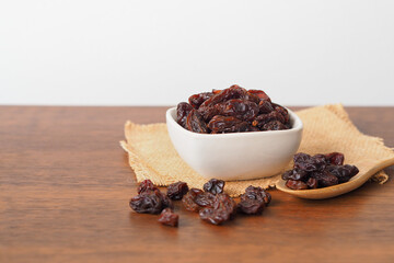 Raisins in white bowl on wooden table background. Dry raisins.