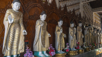 A row of Buddha statues in a Buddhist temple. The sculptures are decorated with golden patterns....