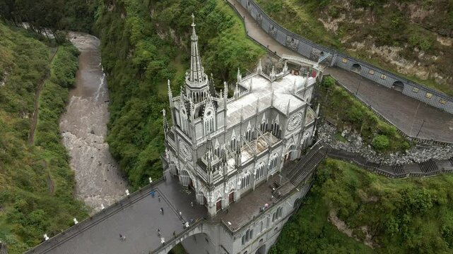 Aerial establishing orbit of Las Lajas Sanctuary spanning a lush canyon in Ipiales, Colombia, surrounded by greenery with rushing river below