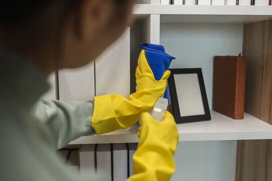 the wife is cleaning her husband home office, cleanup the room, wearing rubber glove to protect her hands, the housekeeper is cleaning the house, tidy up