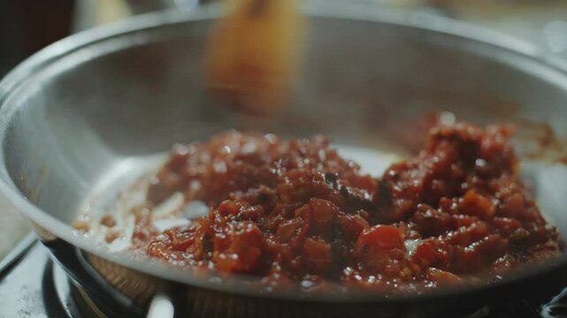 Stirring chopped tomatoes with onions and spices in hot pan with spatula while cooking thick sauce for homemade Indian dish. Close-up view