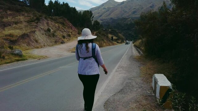 Woman with traditional peruvian hat walks along rural mountain road with cars passing by.. Puka Pukara archaeological ruins surroundings