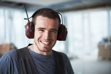 Happy man, portrait or construction engineer with headphones for industry or hearing safety on site. Face, male person or architect with smile for noise canceling earphones or industrial development