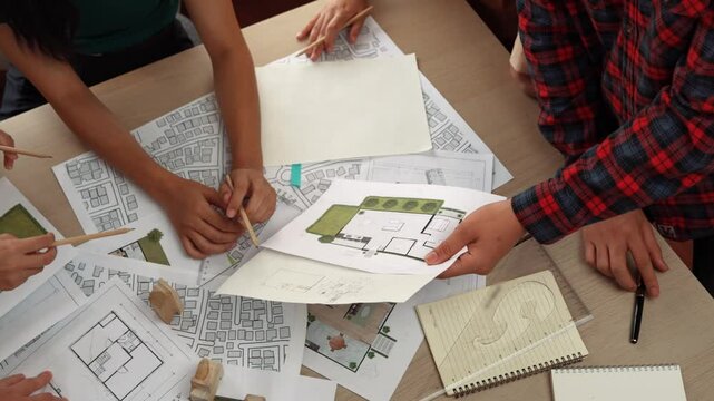 Smart architect and safety engineer discussion about building blueprint on table with architectural document, measurement tools and wooden block scatter around at modern office. Closeup. Delineation.