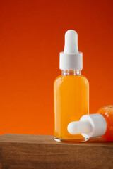 Glass bottle with orange serum on wooden podium. Unmarked container for cosmetic products with vitamin C