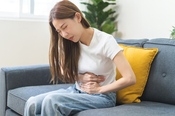 Sick asian young woman in pain, hand holding belly, stomach pain from food poisoning, girl hurt...