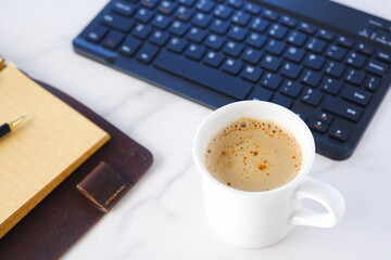 机にリング式のシステム手帳を広げ、淹れたてのコーヒー（カフェ・ラテ）を飲みながら、パソコンでデスクワークをしているイメージ
