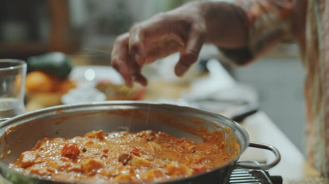 Hands of man squeezing lime juice over paneer butter masala, then stirring ingredients with spatula as cooking Indian food. Close-up shot