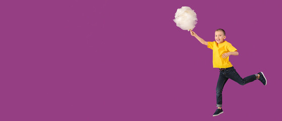 Jumping little boy with cotton candy on color background