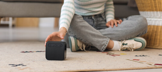Beautiful young woman with wireless portable speaker sitting on floor at home