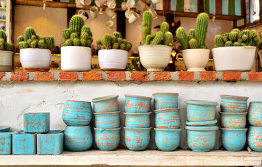 Group of earthenware at shelf and cactus in cup on top of wall