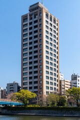 Fototapeta premium Modern urban skyscraper beside river with clear blue sky and lush green trees in the foreground