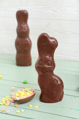 Chocolate Easter egg with sprinkles and bunnies on green wooden table