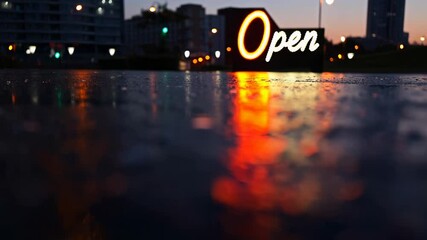 Neon 'Open' sign glowing at night, reflecting on a wet urban surface. A warm and inviting atmosphere in a cityscape after rain