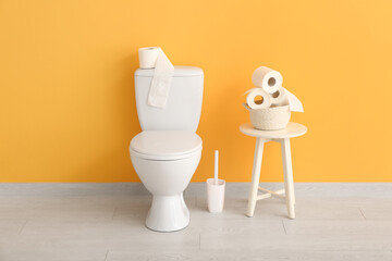 Ceramic toilet bowl, brush and rolls of paper near color wall