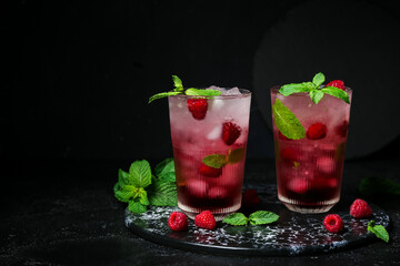 Board with glasses of fresh raspberry mojito on black background