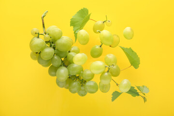 Flying sweet green grapes with leaves on yellow background