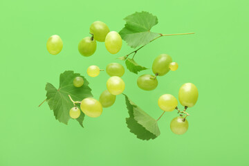 Flying sweet green grapes with leaves on color background