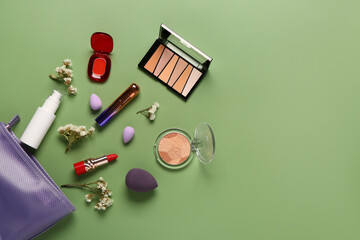 Stylish purple cosmetic bag with makeup products and beautiful flowers on green background