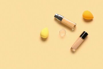 Bottles of makeup foundation with sponges on beige background