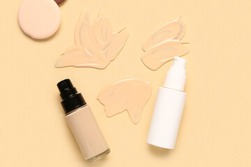 Bottles of makeup foundation with sponges and samples on beige background