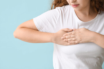 Young woman checking her breast on blue background, closeup. Cancer awareness concept
