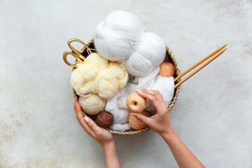 Female hands, basket with yarn balls and knitting needles on grey table