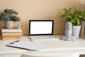 Blank laptop with books and plants on table in office