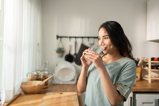 Asian young attractive woman drink a glass of water in kitchen at home. 