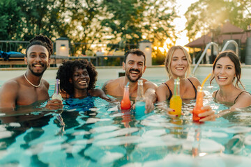 Happy friends enjoying drinks in a swimming pool at sunset