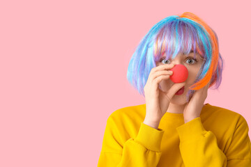Beautiful young woman in funny clown disguise on pink background. April Fools Day celebration
