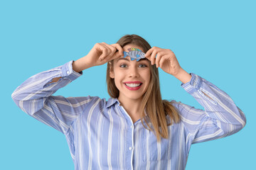 Beautiful young happy woman with paper fish attached to her forehead on blue background. April...