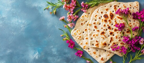 Naklejka premium Freshly baked Jewish flatbread arranged on a blue textured background, surrounded by vibrant pink and purple flowers, creating a rustic natural aesthetic.