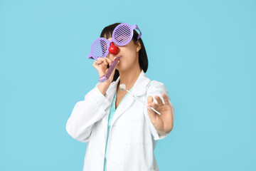 Funny young female dentist with party blower and dental tool on blue background. Fool's day