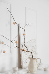 Vase with tree branches, Easter eggs and painting on table near light wall